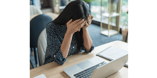 woman with head in hands sitting in front of laptop